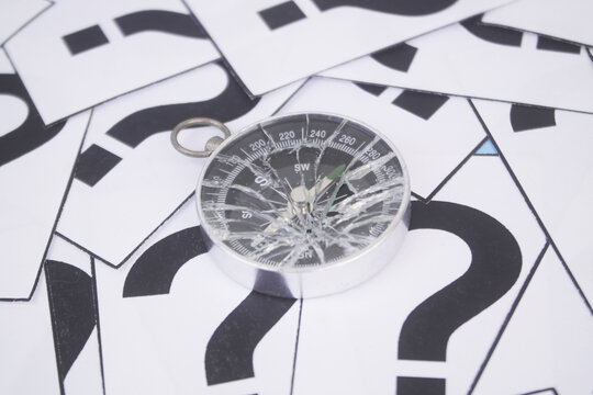 Broken compass on question marks background.	