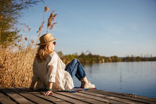 Woman relaxing on pier at lake. Tranquil solitude moment in nature, digital detox and mindful slow living