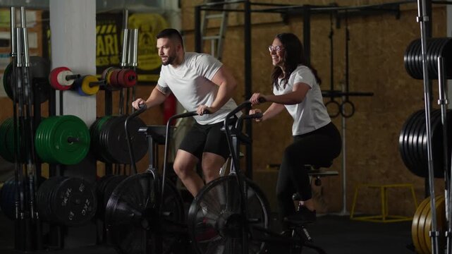 Athletic couple doing cardio training on air bikes in a gym