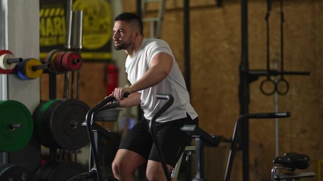 Muscular man performing intense cardio on an air bike