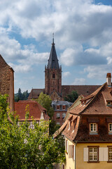 Obraz premium Wissembourg shows a view of the Abbey Sts Peter and Paul church tower and buildings with trees and clouds above.