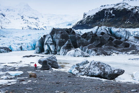 Hiker looking at a large melting ice block at Sv&iacute;nafellsj&ouml;kull, Iceland