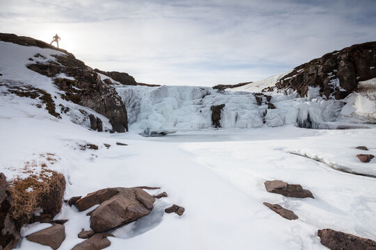A figure stands silhouetted at the top of a frozen waterfall, Iceland