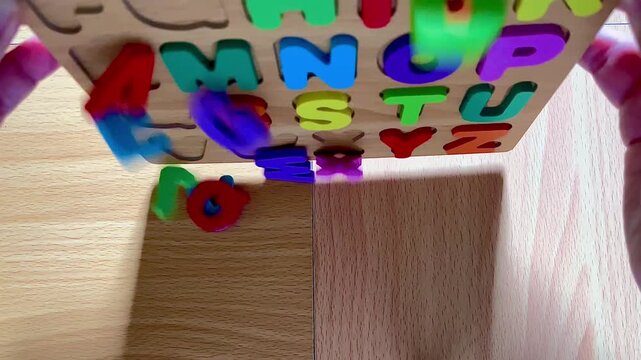 Hands Dumping Colorful Wooden Alphabet Puzzle Letters from a Board onto a Table