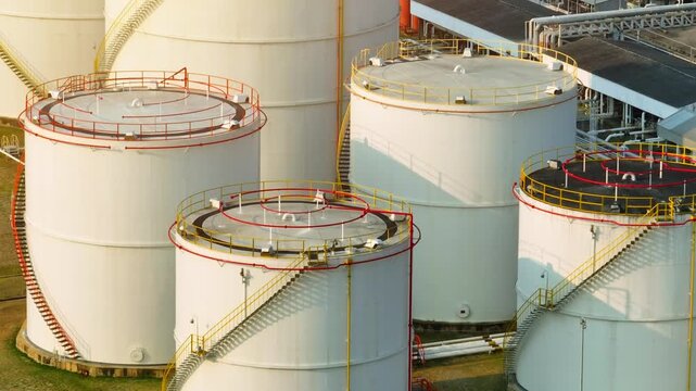 Aerial drone view of oil storage tanks with circular tops and metal stairways, reflecting global energy reserves and the strategic importance of fuel storage amid ongoing supply uncertainties.
