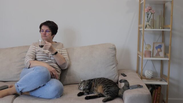 Woman drinking wine on sofa with sleeping cat