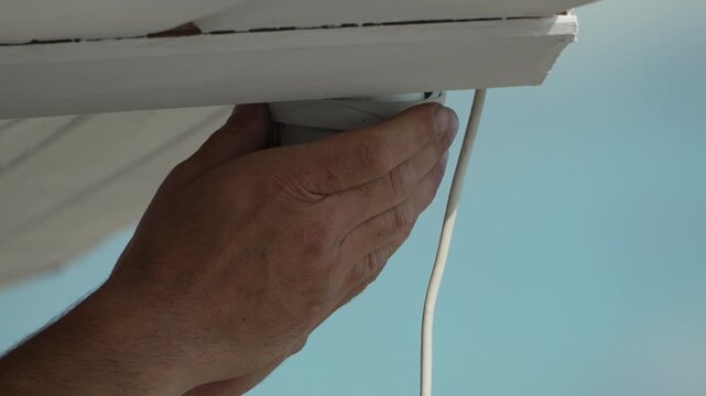 Light bulb, installation, hands screwing an energy-efficient LED light bulb into a socket under a white house eave.