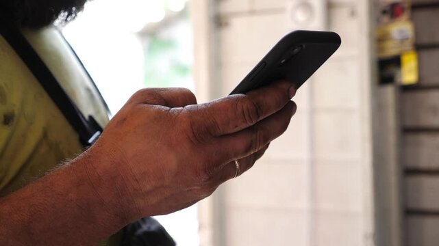 Mechanic using smartphone to check vehicle information in a well-lit garage, showcasing the integration of technology in automotive service and repair processes