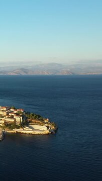 Aerial view of the seaside village of Paralio Astros, Greece, featuring an open-air amphitheater and traditional houses along the coastline with mountains in the background.