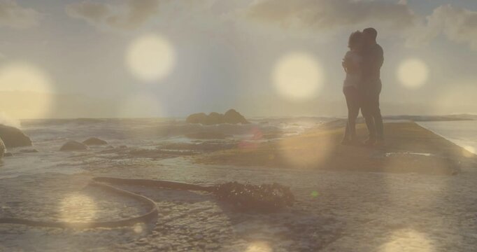 Couple embracing rock sun lowering causing bokeh on silhouette while camera pulling back for travel