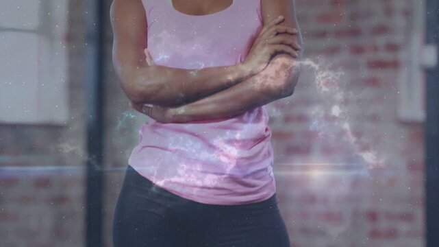 Stepping trainer entering gym, planting feet and crossing arms, wearing pink top with nebula effect