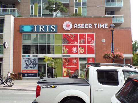 Ottawa, Ontario, Canada &ndash; July 23, 2025: An urban storefront in Westboro features "IRIS optometry and Aseer Time" dessert shop signage at 438 Richmond Road.