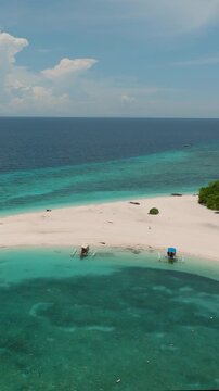 Flying over the white beach with turquoise water in Mantigue Island. Blue sky and clouds. Camiguin, Philippines. Vertical video.