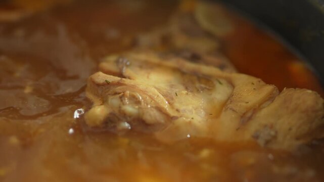 Close-up of pork hock simmering in reddish broth in pot