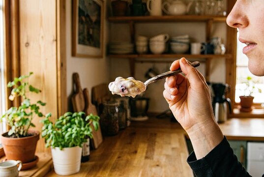 Hand holding a spoon filled with creamy skyr, about to eat, in a wholesome kitchen with warm light