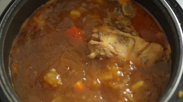 Close-up of pork hock simmering in reddish broth in pot