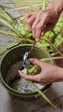 Close up of hands filling woven palm leaf pouches with uncooked rice to make traditional ketupat dumplings for Eid al-Fitr celebrations