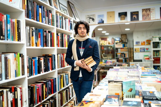 Young man holding books in a second-hand bookstore aisle