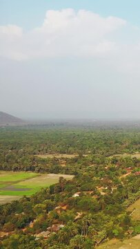 Aerial view of a vibrant green countryside with scattered houses and fields near Baray Occidental, under a partly cloudy sky.