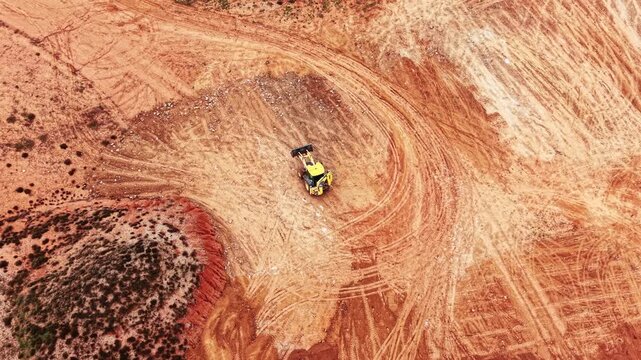 Small yellow excavator moves by the sandy area. Modern equipment working in the quarry. Aerial view.