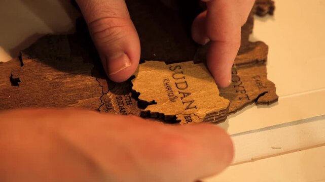 An unrecognizable man glues a wooden world map of countries cut out of plywood. The creative process of creating DIY crafts from above. Assembling a puzzle. Hobby concept. High quality 4K footage.
