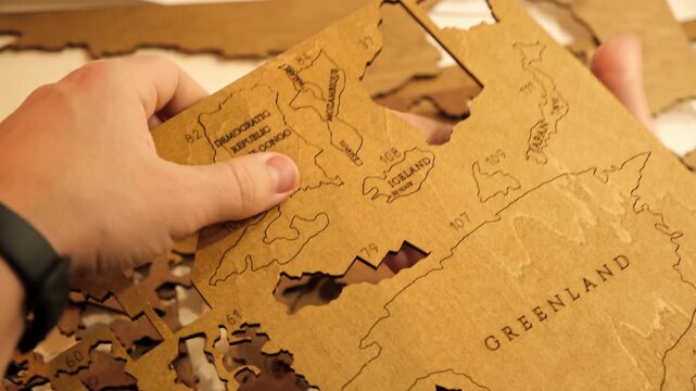 Male hands take out a laser-cut piece from a sheet of plywood to assemble a decorative wooden world map. The creative process of creating DIY crafts. Hobby concept. Carpentry. High quality 4K footage.