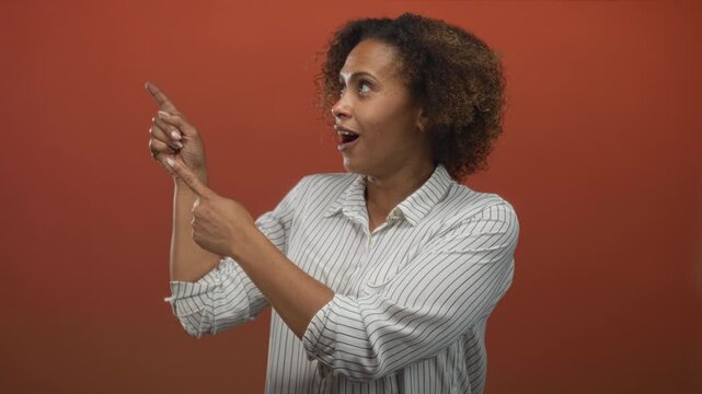 Woman pointing finger and looking upward in studio with orange backdrop; surprise curiosity amazement.
