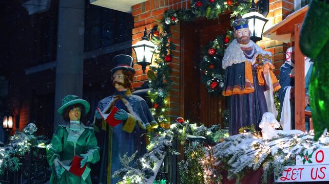 Figures of carol singers are moving in the nativity scene. Snowy night on Christmas season.