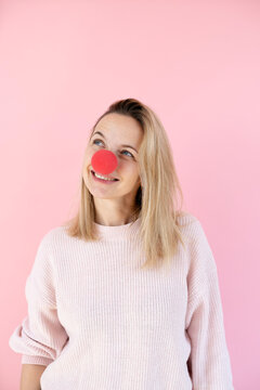 blond woman in front of pink background with red clown nose