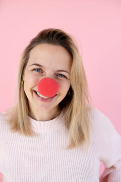 blond woman in front of pink background with red clown nose