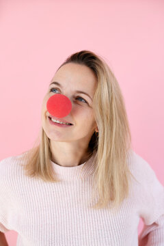 blond woman in front of pink background with red clown nose