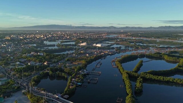 Aerial morning hyperlapse over a bustling coastal city, featuring traffic on a river bridge, extensive aquaculture fish pens, and distant mountains in Dagupan, Pangasinan, Philippines