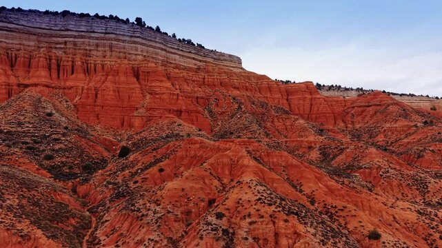 Red clay cliffs with white sedimentary layers in Teruel Spain. Side view of eroded red sandstone cliffs topped with white limestone layers under a blue sky in Spain.