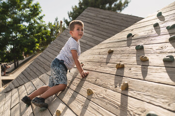 A 5-6 year old boy learns to climb on a rock climbing wall in a park during the summer. Climbing for kids © illustrissima