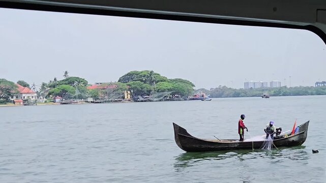 Traditional wooden boat with fishermen on Kochi's backwaters in Kerala. Bolgatty Palace is visible on the lush shoreline. The scene captures the serene, local lifestyle against a scenic island backdro