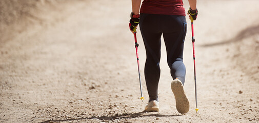 Senior woman walking in forest with Nordic walking sticks, sunny summer day. An active lifestyle in retirement, a hike in nature
