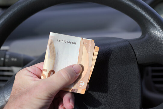 male hand holding folded euro notes inside a car