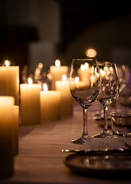 Lots of wine glasses and candles on tables set for dinner in the evening.