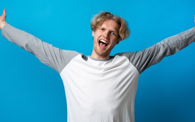 Naklejka premium Excited young man with outstretched arms celebrating success, expressing happiness and joy on blue background, feeling triumph and achieving goals