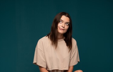 Obraz premium Young woman making a goofy facial expression with tongue out, looking sideways, playful and humorous on teal background