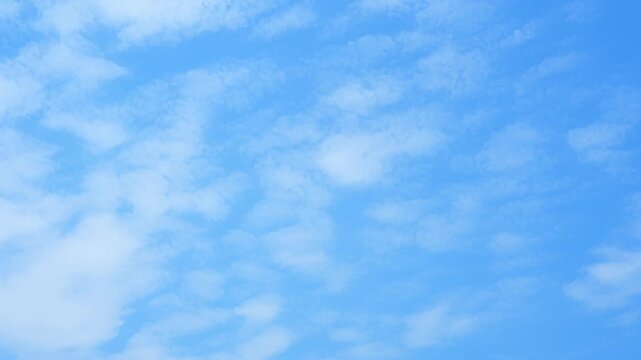 A blue sky timelapse video footage with soft textured clouds spreading across a bright atmosphere, showing gentle cloud movement, natural light variation, and a peaceful, airy sky background.
