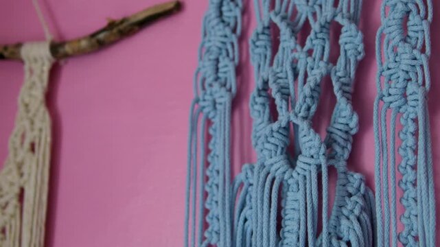 Handmade macrame wall decor on pink rural house wall with traditional woven patterns creating cozy boho atmosphere and authentic countryside interior style