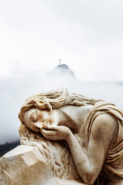 Sculpture of a woman reclining on a stone, with a serene and melancholic expression, at the feet of Christ. Necrotourism. Artist unknown, S&atilde;o Jo&atilde;o Batista Cemetery, Rio de Janeiro, Brazil.