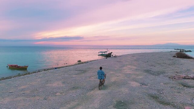 Man Riding a Bicycle on a Tropical Beach During a Vibrant Sunrise.