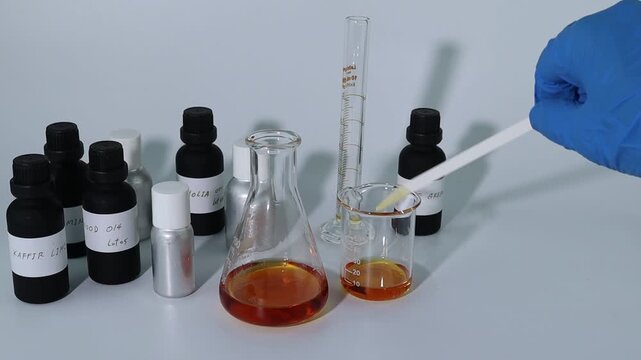 chemical beaker , flask is on white table with blotting paper , fragrance bottle and essential oil bottle are used to blend the nice scent for making perfume and candle by perfumer in the laboratory