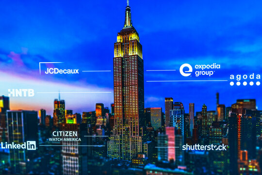 Empire State Building night skyline with visible corporate logos and illuminated New York cityscape. New York. USA.