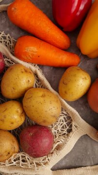 Variety of garden fresh vegetables like potatoes, carrots, and an onion in an eco friendly string bag