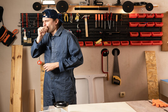 carpenter man with diy tools for maintenance and repair work dealing with flu symptoms, coughing in workshop. Woodworking and carpentry