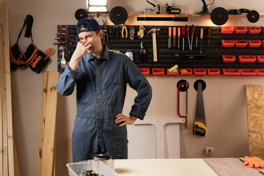 Carpenter man with diy tools for maintenance and repair work closing his nose repulsed by unpleasant odor in workshop. Woodworking and carpentry. Terrible smell