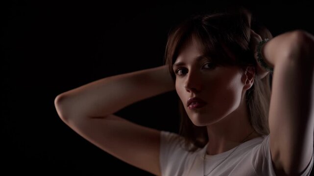 Self-care and beauty A woman ties her hair up in a dark studio captured in slow motion commercial use in beauty product advertisements fashion editorials or wellness promotions The clip highlights.